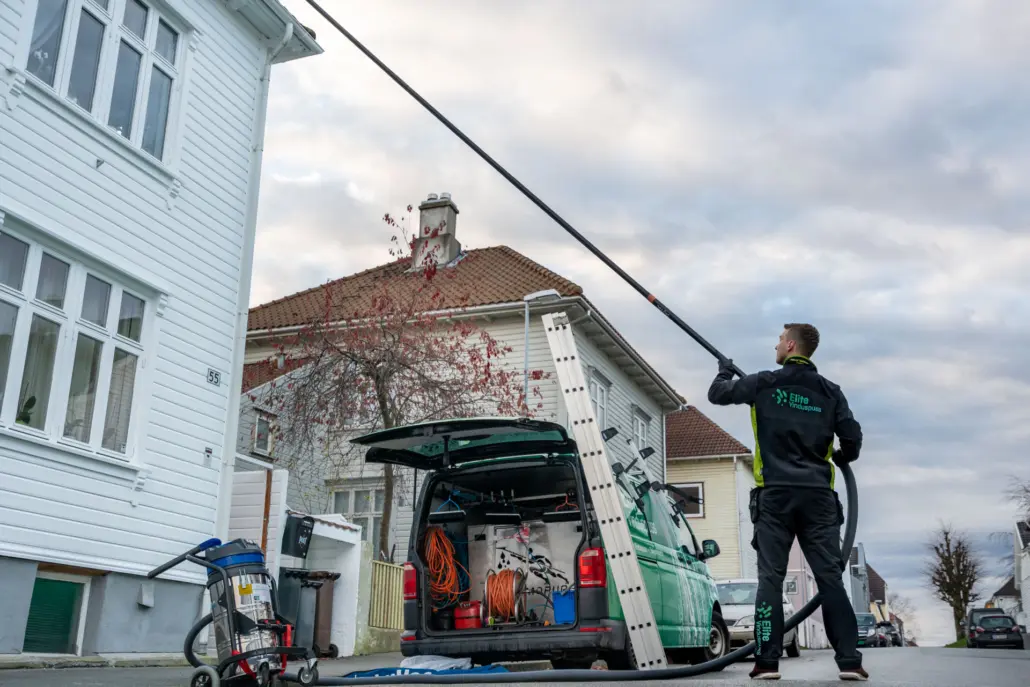 Person som vasker fasade og takrenner på et hvitt hus.