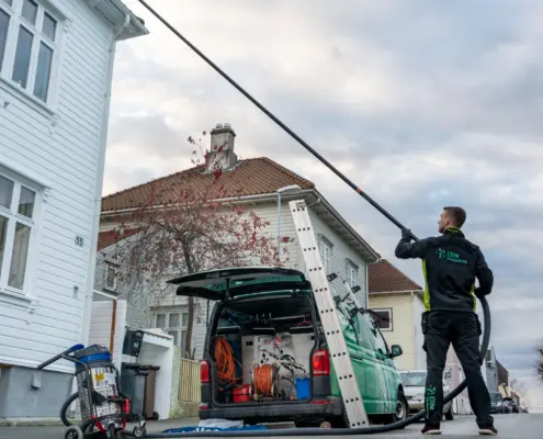 Person som vasker fasade og takrenner på et hvitt hus.
