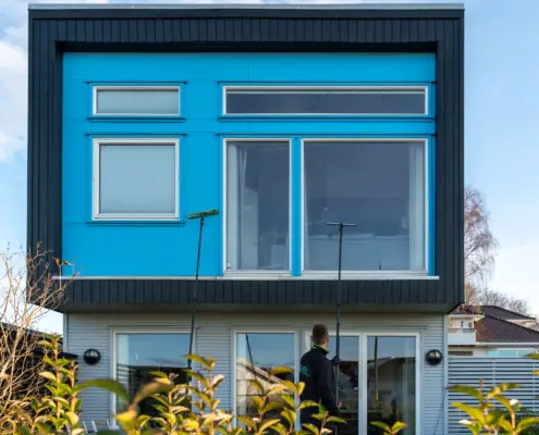 Ansatt i Elite Vinduspuss som vasker vinduer på et hus med blå plater.